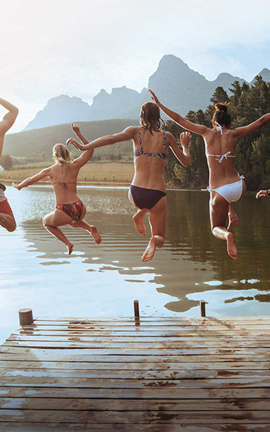 Junge Leute springen vor einer Bergkulisse von einem Steg in den See